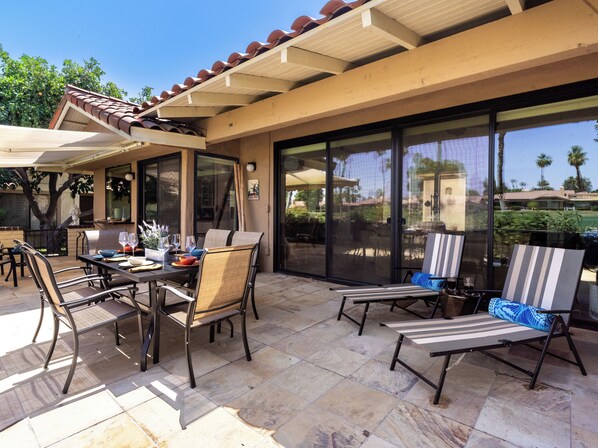 An outdoor patio with a table set for dining, chairs, and a covered seating area. - Country Club Condo w/ Fairway Views + 37 Pools (Palm Desert)