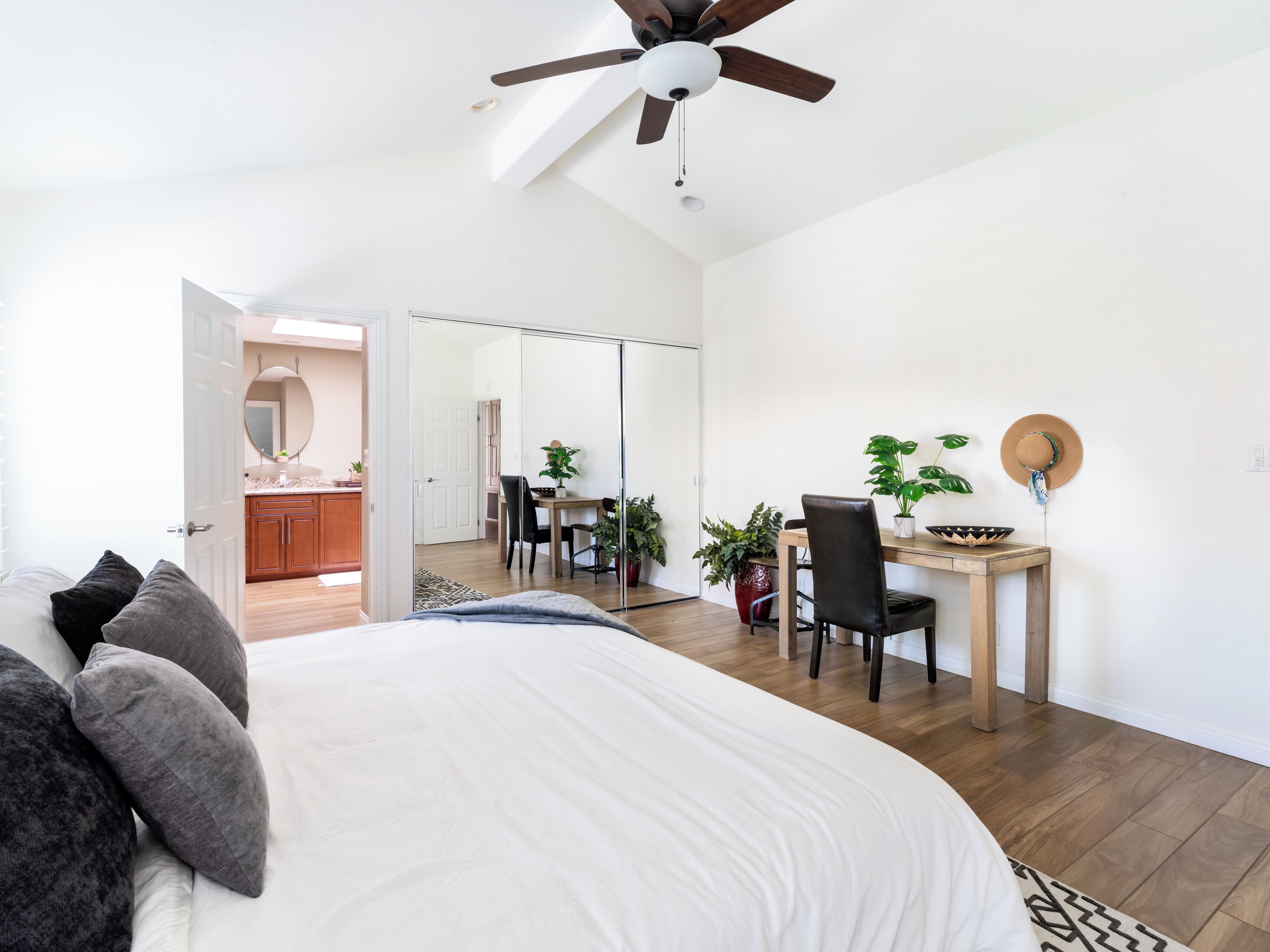 Un dormitorio con cama, escritorio y silla. Hay un ventilador de techo y un espejo en la pared.