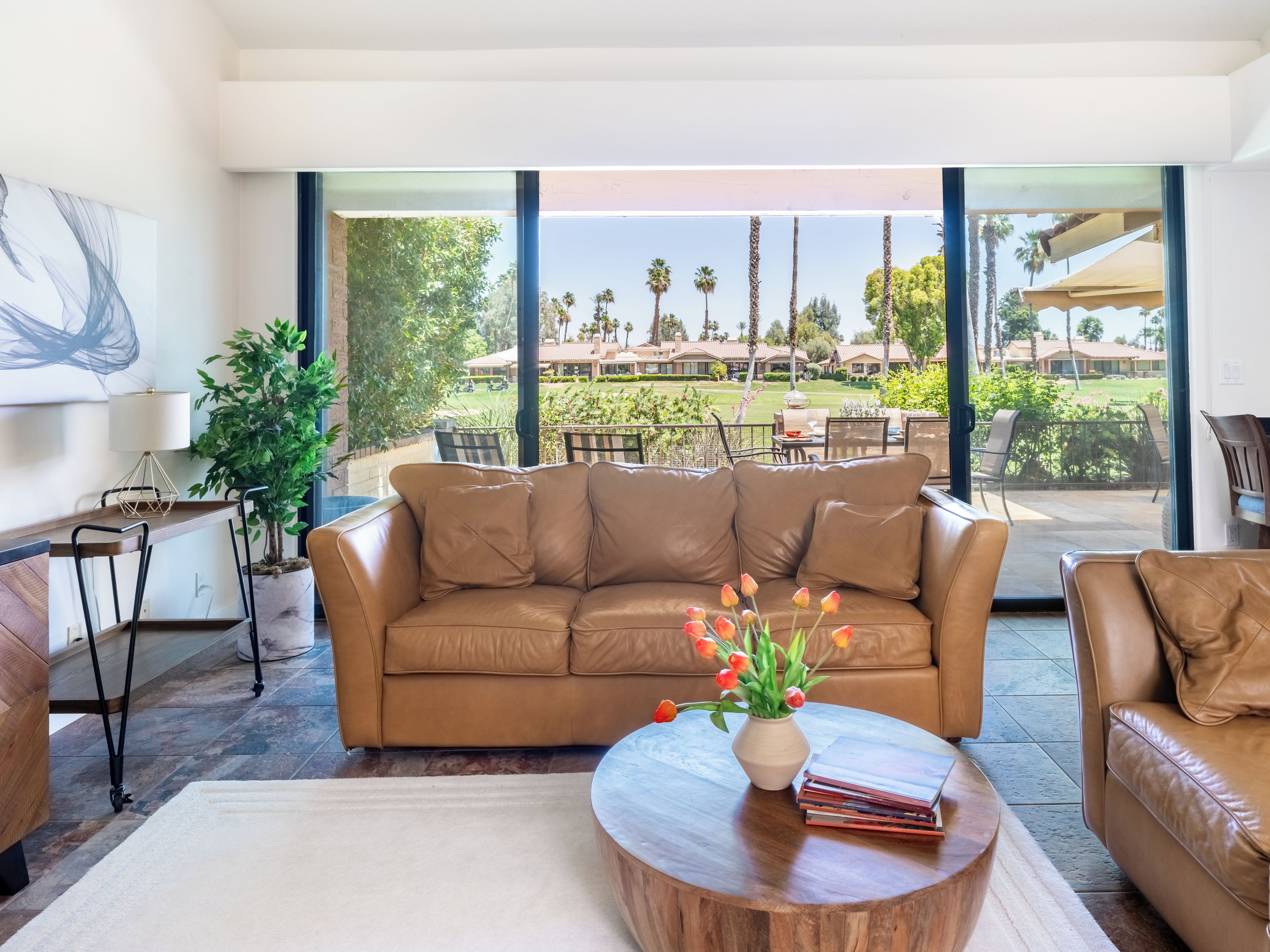 A modern living room with a leather sofa, a wooden coffee table, and a view of a landscaped outdoor area.