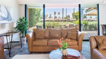 A modern living room with a leather sofa, a wooden coffee table, and a view of a landscaped outdoor area.