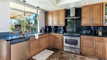 A modern kitchen with wooden cabinets, a stainless steel range, and a large window overlooking greenery.
