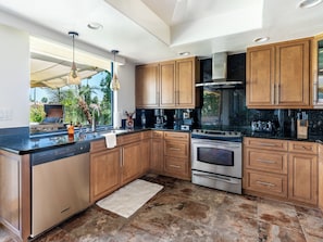A modern kitchen with wooden cabinets, a stainless steel range, and a large window overlooking greenery. - Country Club Condo w/ Fairway Views + 37 Pools (Palm Desert)