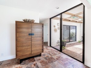 A modern interior with a wooden cabinet, a sliding glass door leading to an outdoor patio, and a tiled floor. - Country Club Condo w/ Fairway Views + 37 Pools (Palm Desert)