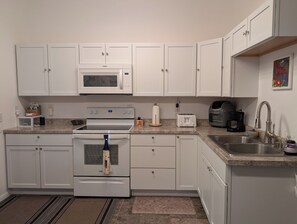 A kitchen with white cabinets, a microwave, a stove, a toaster, and a coffee maker.
