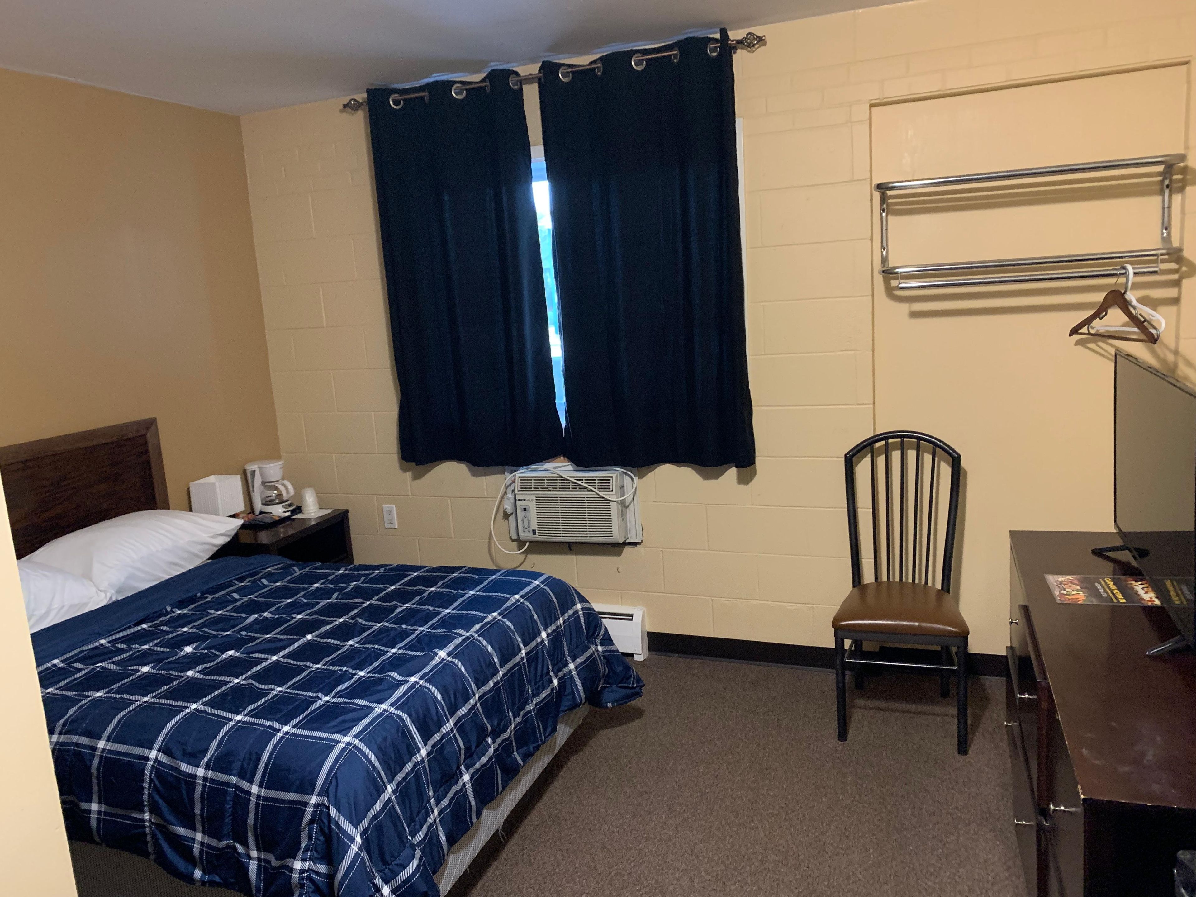 Quarto de hotel com cama, cadeira, escrivaninha, espelho, aquecedor e janela com cortinas.
