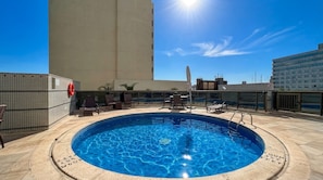 Una piscina en la azotea con un cielo azul despejado, rodeada de sillas de descanso y un flotador.