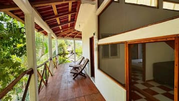 A covered outdoor area with a wooden deck, a bench, and a view of greenery.
