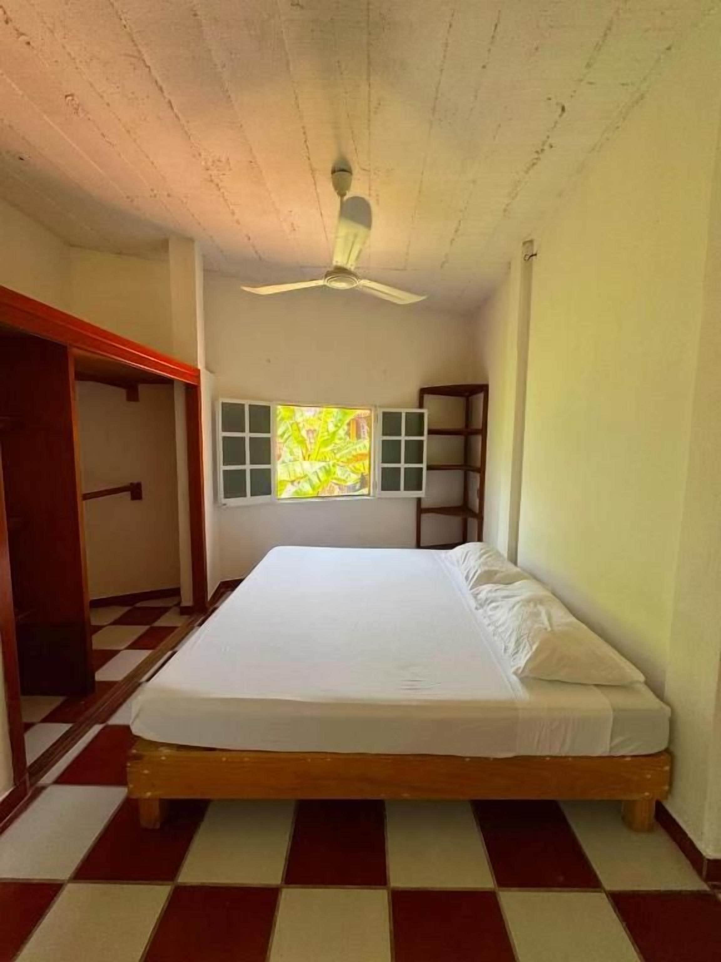 Une chambre avec un lit, un ventilateur de plafond, une fenêtre donnant sur un beau paysage et un sol à carreaux.