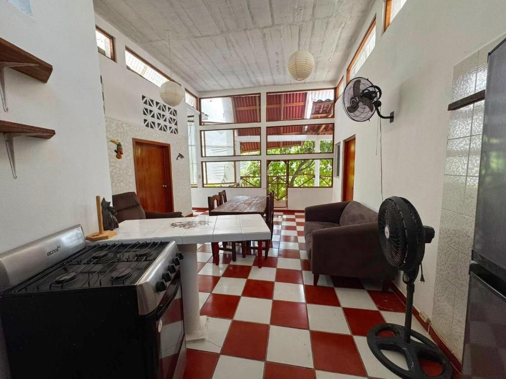 Uma cozinha com fogão a gás, mesa de jantar com cadeiras, piso xadrez e um ventilador.
