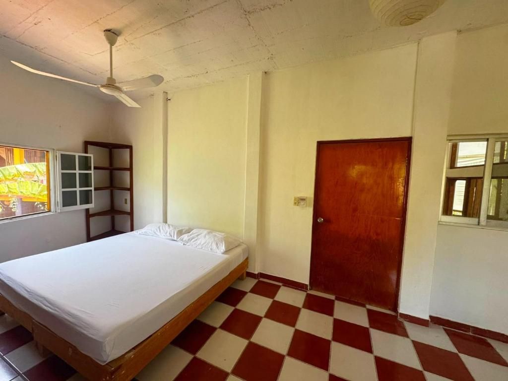 A room with a bed, a ceiling fan, a checkered floor, a door, and a window.