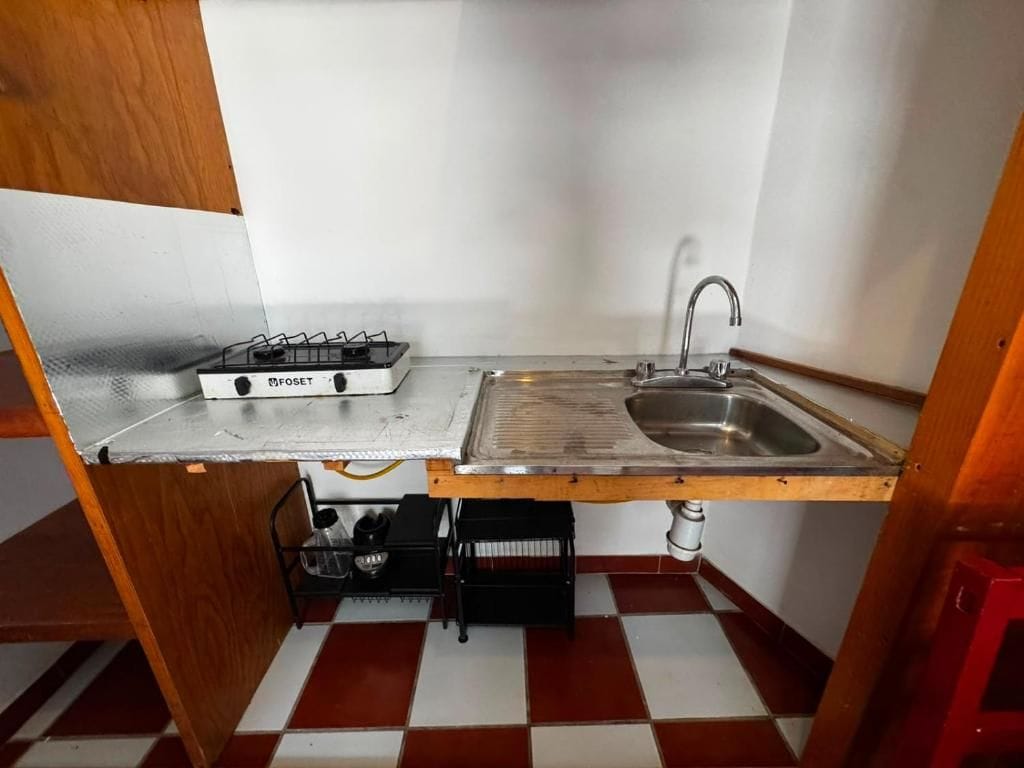 Una cocina compacta con estufa a gas, lavamanos y piso a cuadros.