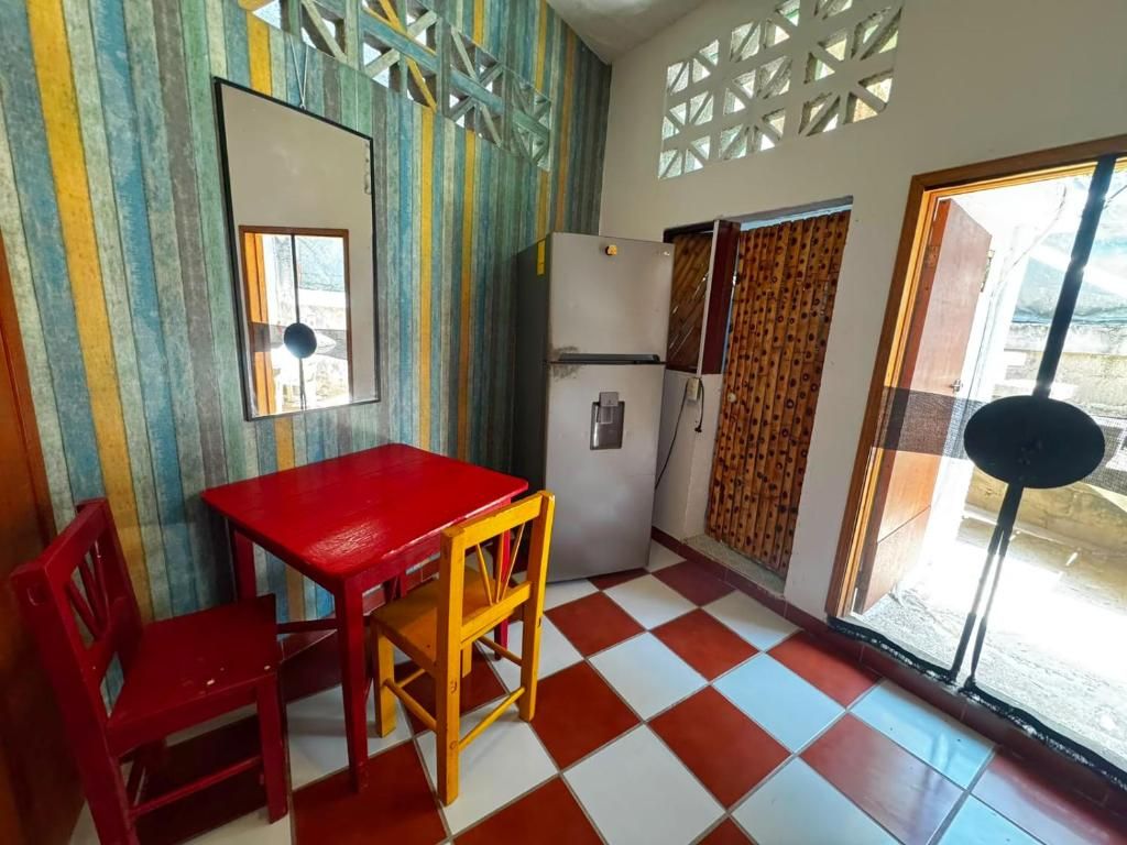A kitchen with a red table and chairs, a refrigerator, and a window with patterned curtains.