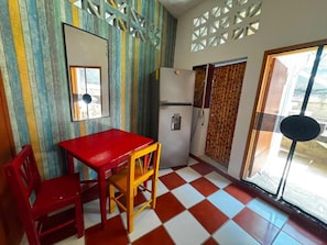 Una cocina con una mesa y sillas rojas, un refrigerador y una ventana con cortinas estampadas.