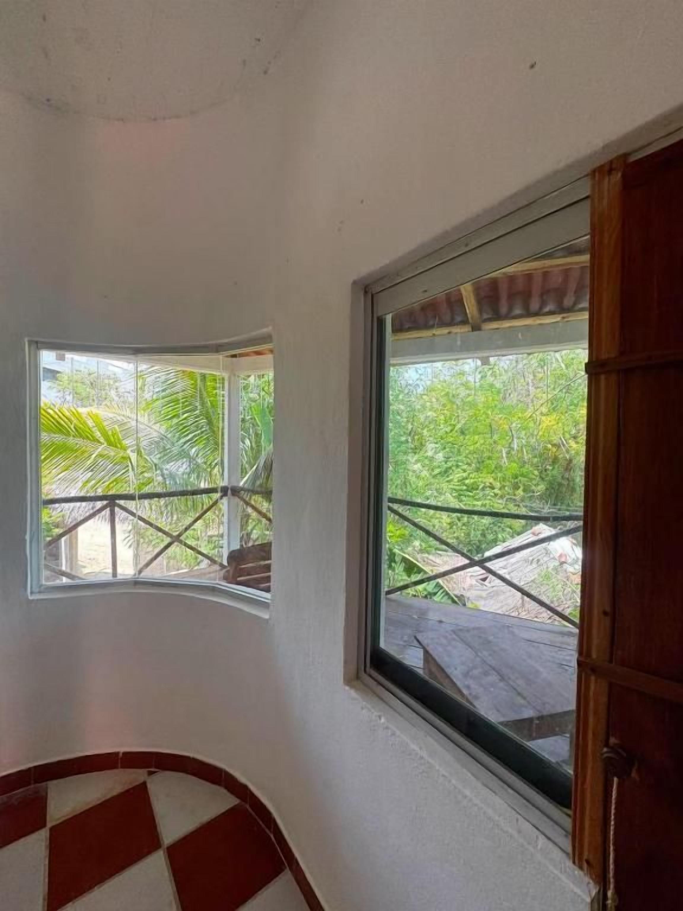 A room with a checkered floor, a window with a view of greenery, and a wooden door.