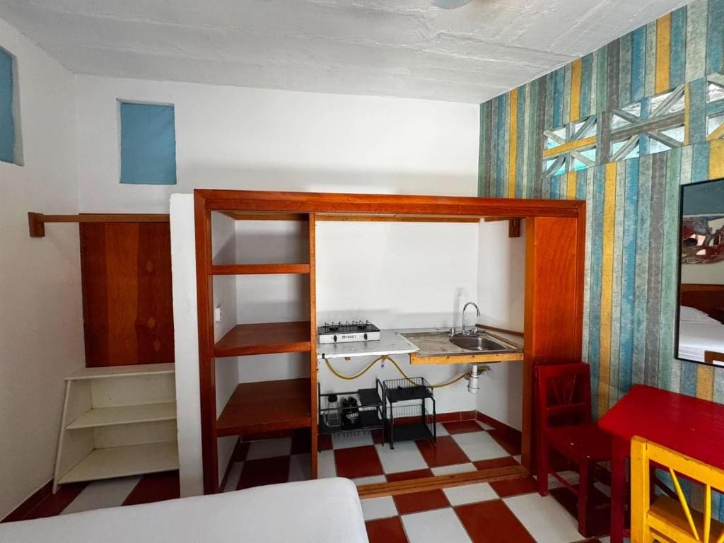 A compact room with a kitchenette, a bed, a chair, and a small table.