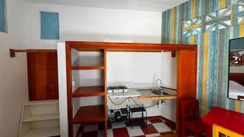A compact room with a kitchenette, a bed, a chair, and a small table.