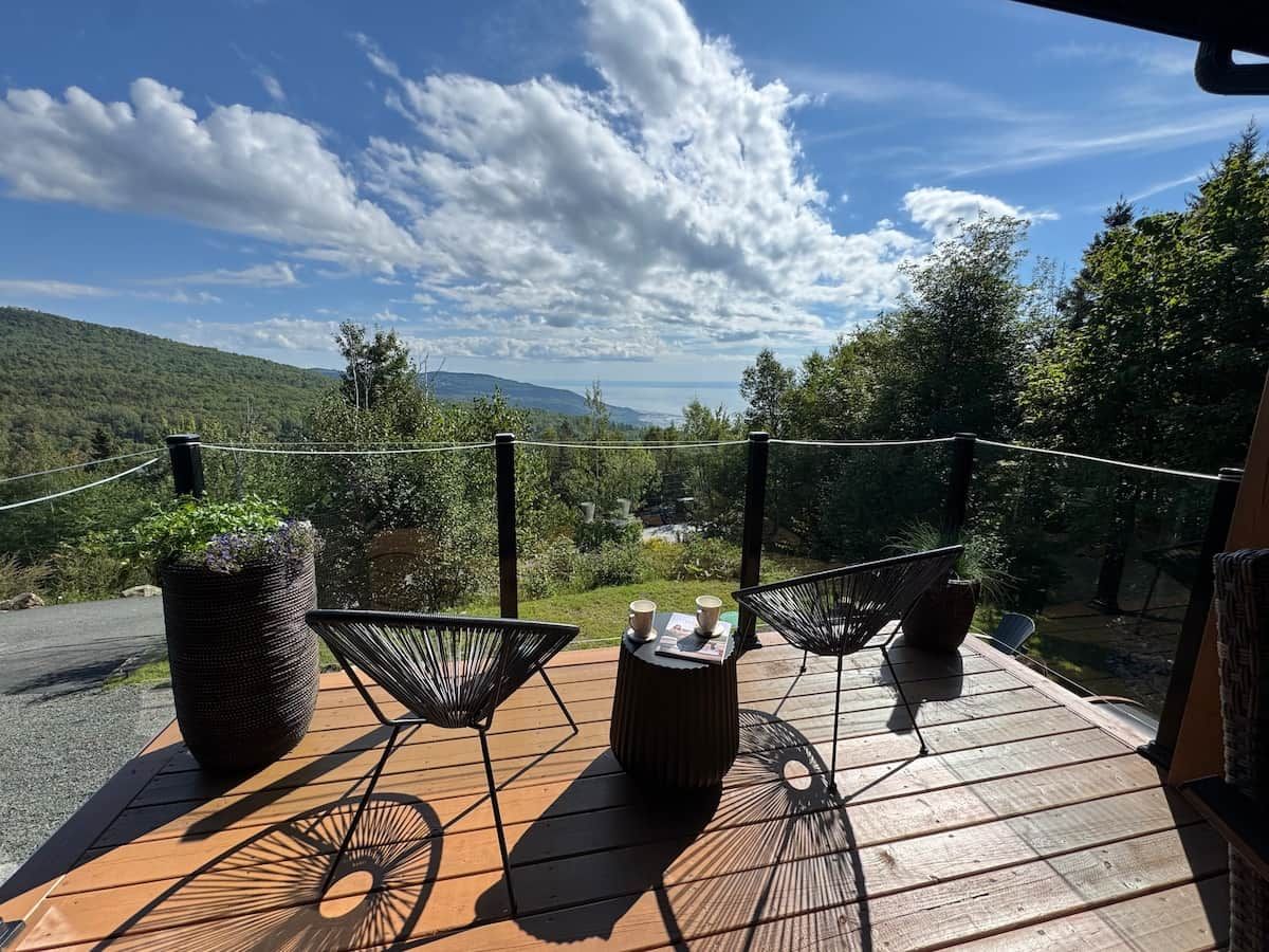 A wooden deck with two chairs and a table, overlooking a scenic landscape with trees and hills.