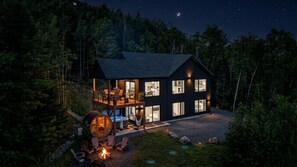 Une cabane moderne à deux étages, dotée d’une terrasse et entourée de forêt.