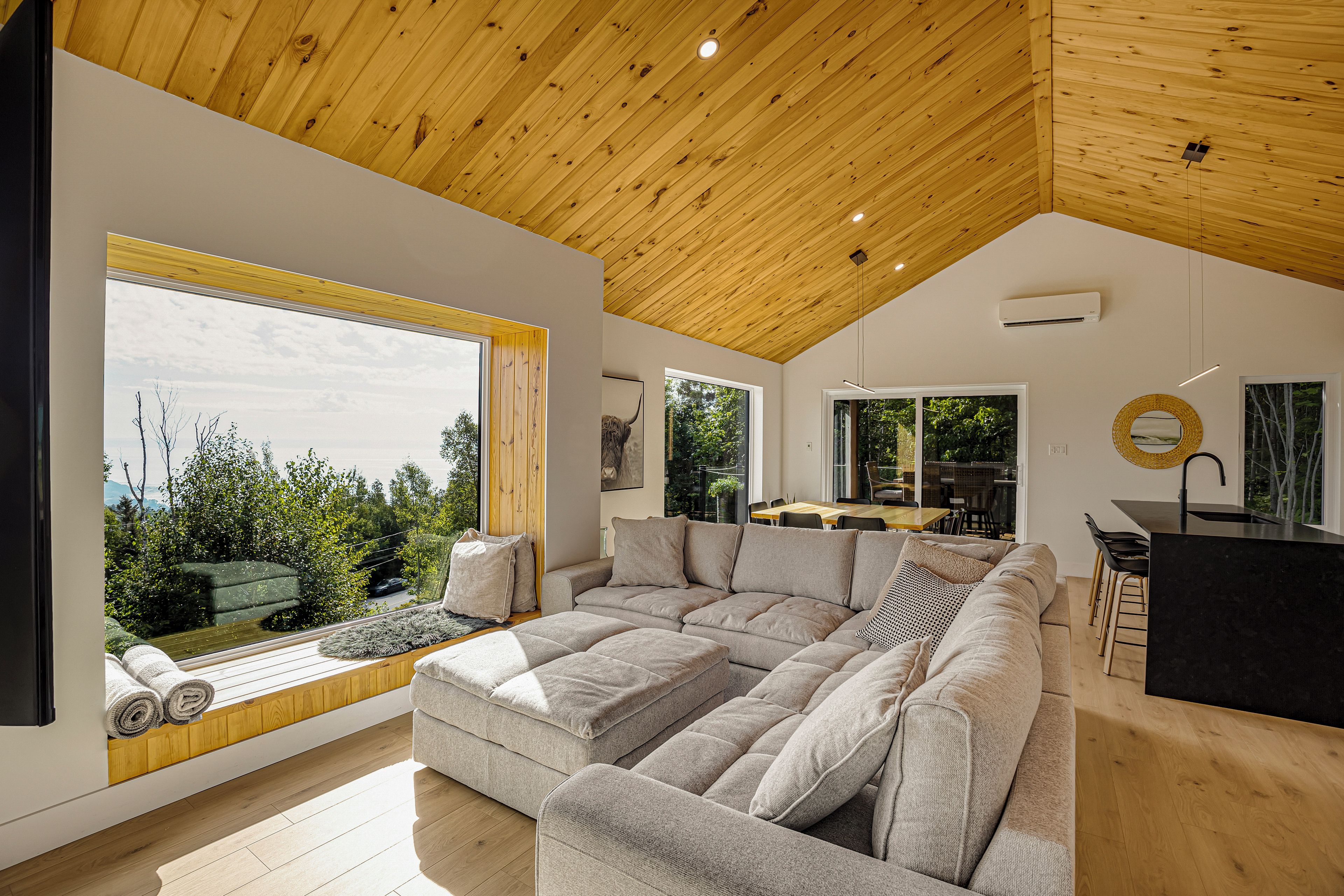 A modern interior with a large sectional sofa, a dining area, and a view of the outdoors.