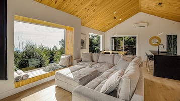 A modern interior with a large sectional sofa, a dining area, and a view of the outdoors.
