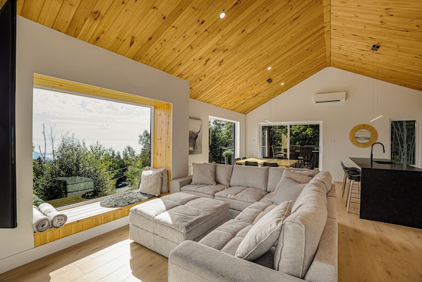 A modern interior with a large sectional sofa, a dining area, and a view of the outdoors.