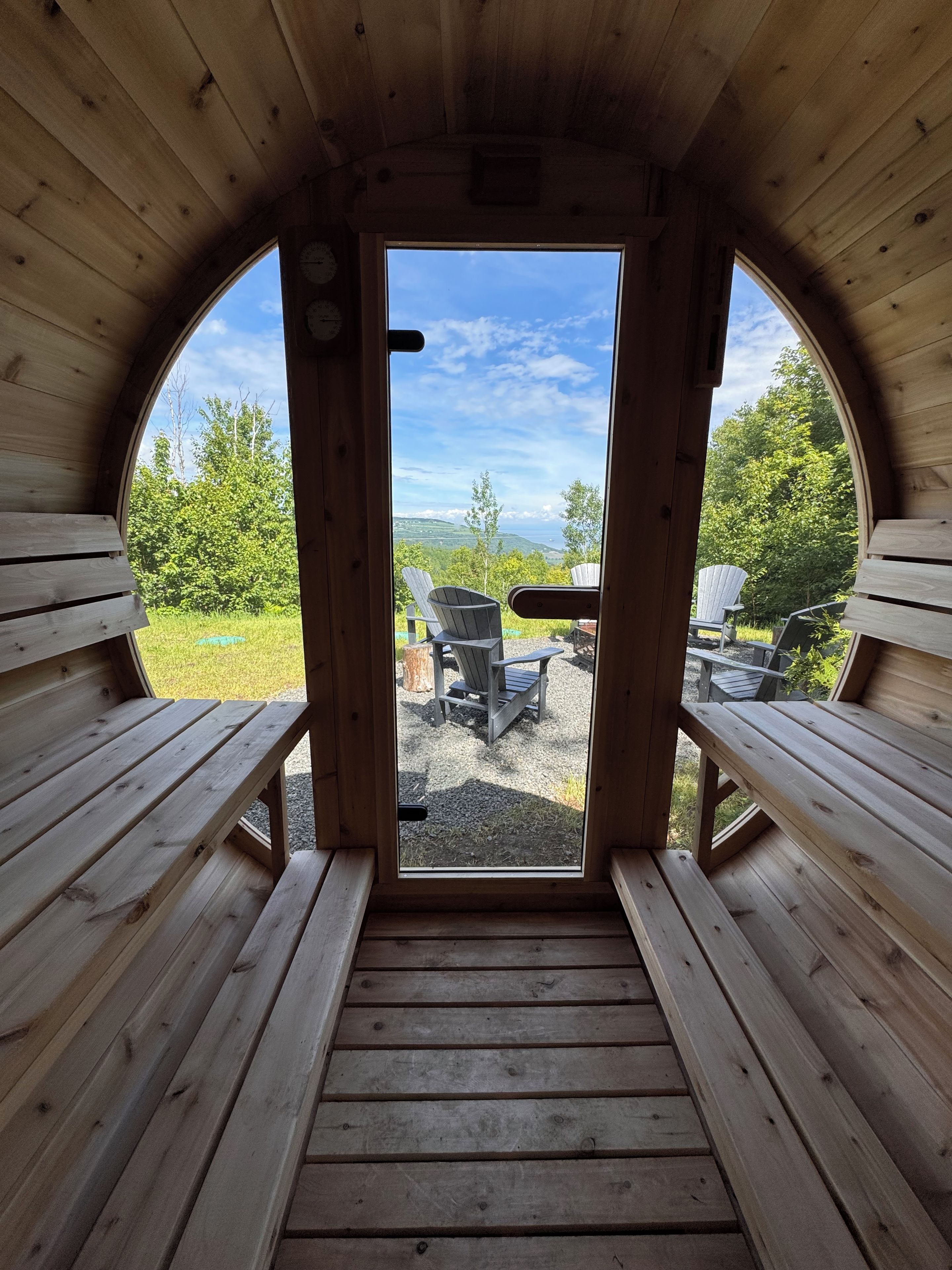 A wooden cabin with a bench and a table in the center, leading to an outdoor seating area with Adirondack chairs.