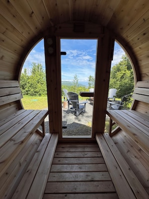 A wooden cabin with a bench and a table in the center, leading to an outdoor seating area with Adirondack chairs.