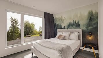 A bedroom with a large window, a bed with a headboard, and a wall-mounted light fixture.