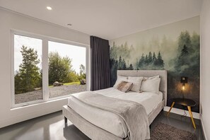Un dormitorio con un ventanal grande, una cama con cabecera y una lámpara fijada a la pared.