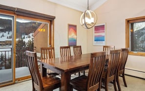 A dining area with a wooden table and chairs, large windows with a view of a snowy landscape, and a hanging light fixture. - Superb 4-bedroom  ski condo at Copper Mountain Resort, Colorado for your getaway (Frisco)