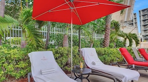 A poolside area with lounge chairs, a red umbrella, and a small table with a drink. - 2BR Beachwalk Resort APT- Intracoastal Views (Hallandale Beach)