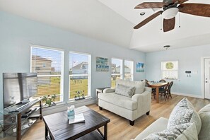 A spacious living room with a ceiling fan, a dining area, and large windows with blinds.