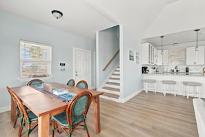 A modern kitchen with white cabinets, a wooden staircase, and a dining area with a wooden table and chairs.