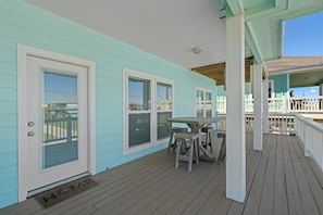 A covered porch with a wooden table and chairs, a door with a window, and a railing.