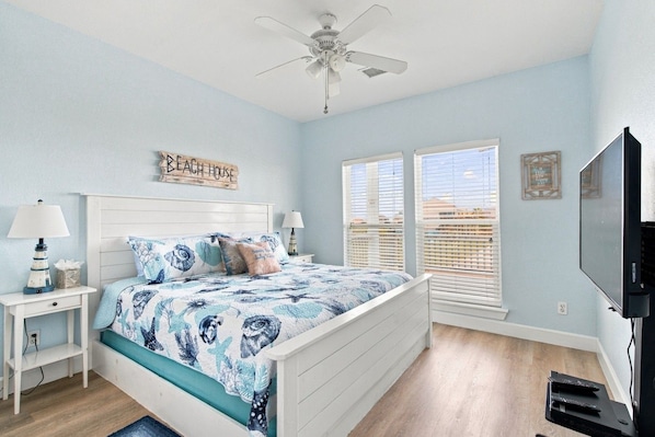 A bedroom with a bed, nightstands, a ceiling fan, a TV, and a window with blinds.