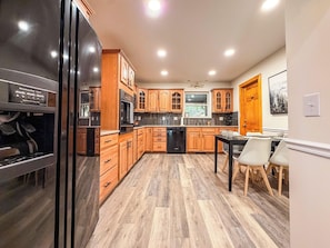 A kitchen with wooden cabinets, a black refrigerator, and a dining area with a table and chairs. - Sunset Mtn Views + Sauna, Whirlpool Tub, Game Room (Bryson City)