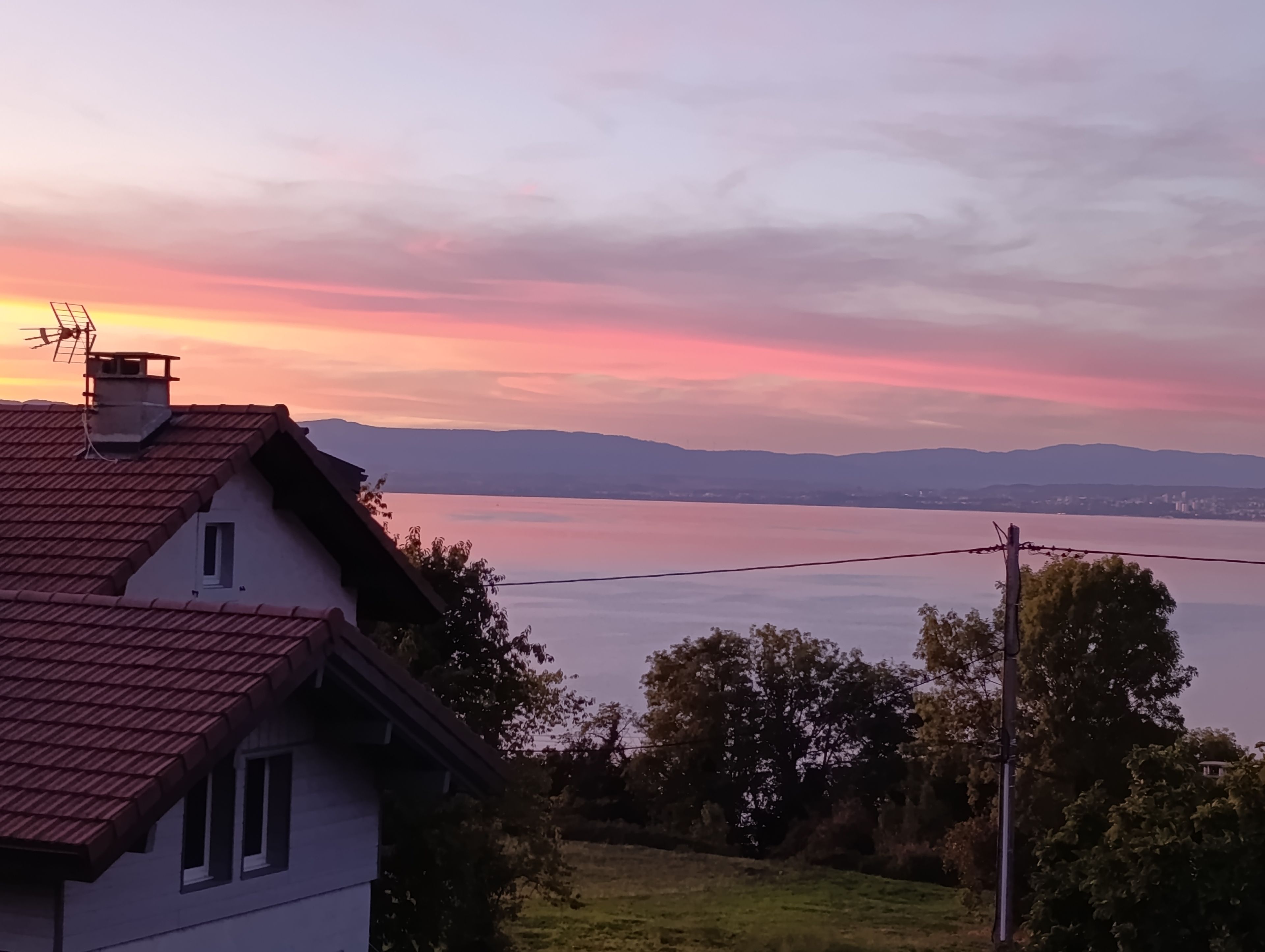 A house with a red-tiled roof overlooking a body of water and distant mountains.