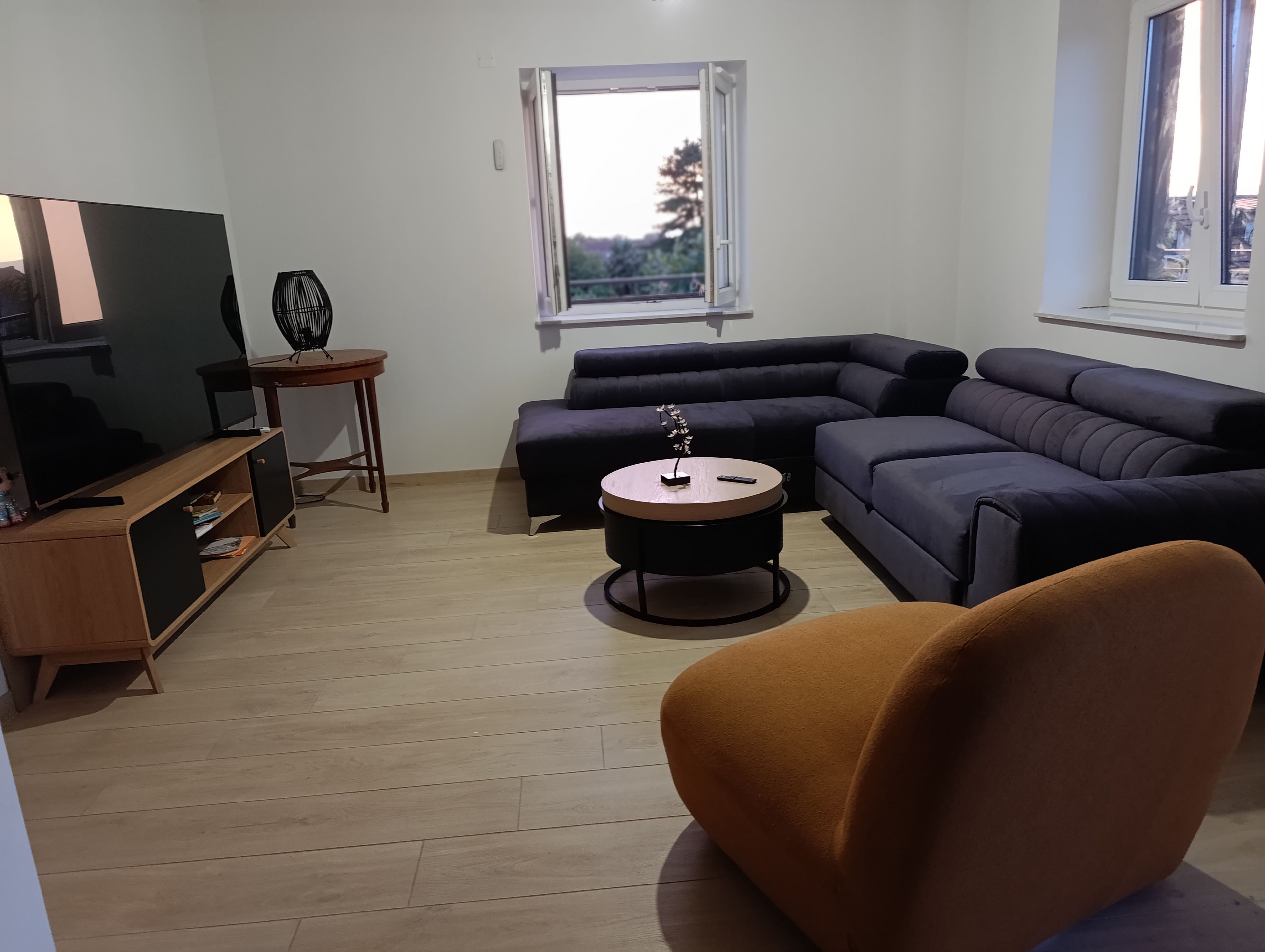 A modern living room with a sectional sofa, a round coffee table, a television, and a small side table.