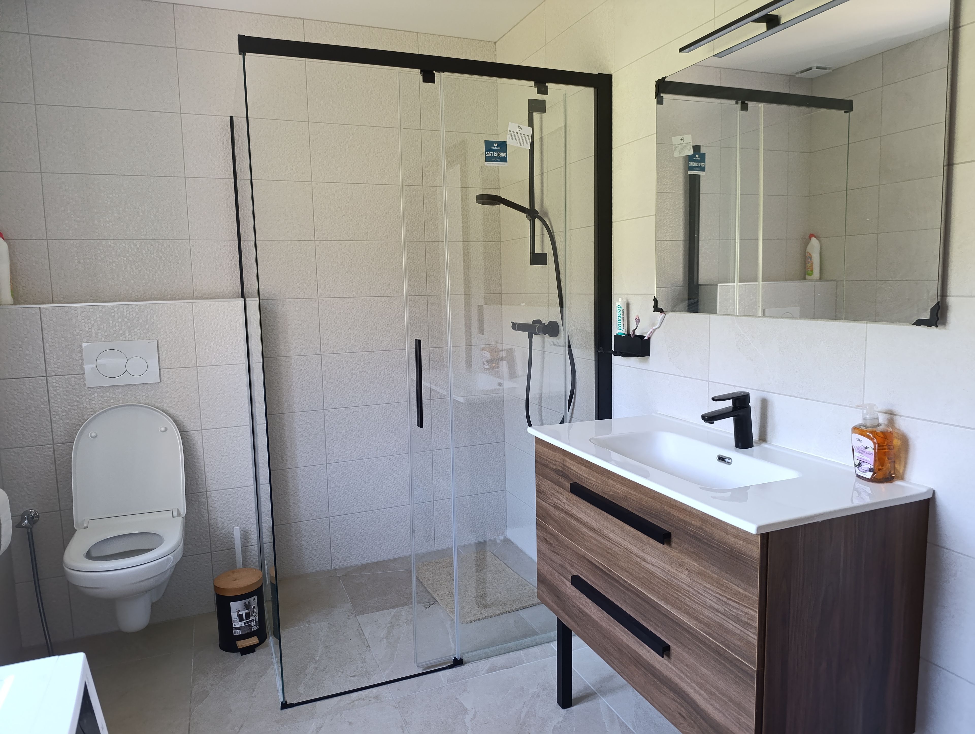 Une salle de bain moderne avec une douche à parois de verre, des toilettes blanches et un meuble-lavabo en bois avec un évier.