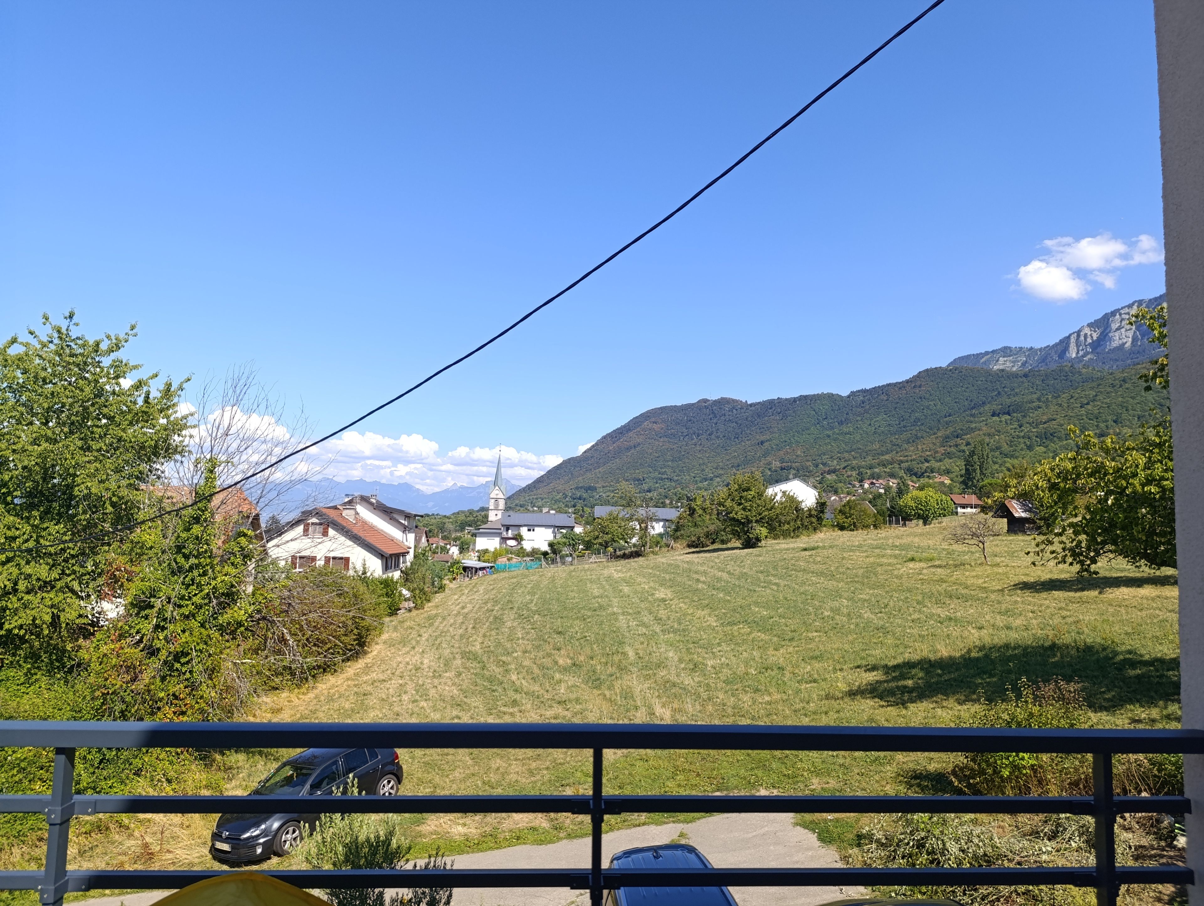 A rural landscape with a church, houses, and mountains in the background.