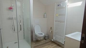 Un baño con cabina de ducha de vidrio, inodoro, radiador y piso de madera.