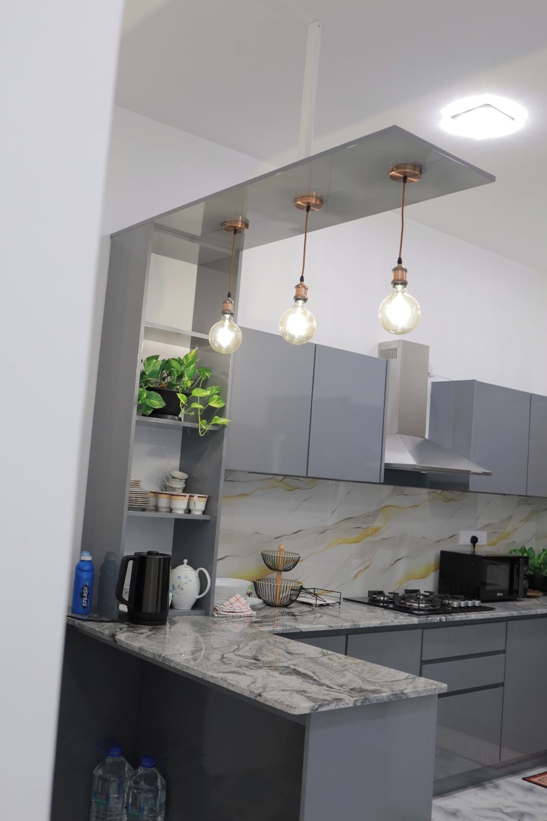 A modern kitchen with grey cabinets, a marble countertop, and pendant lighting.