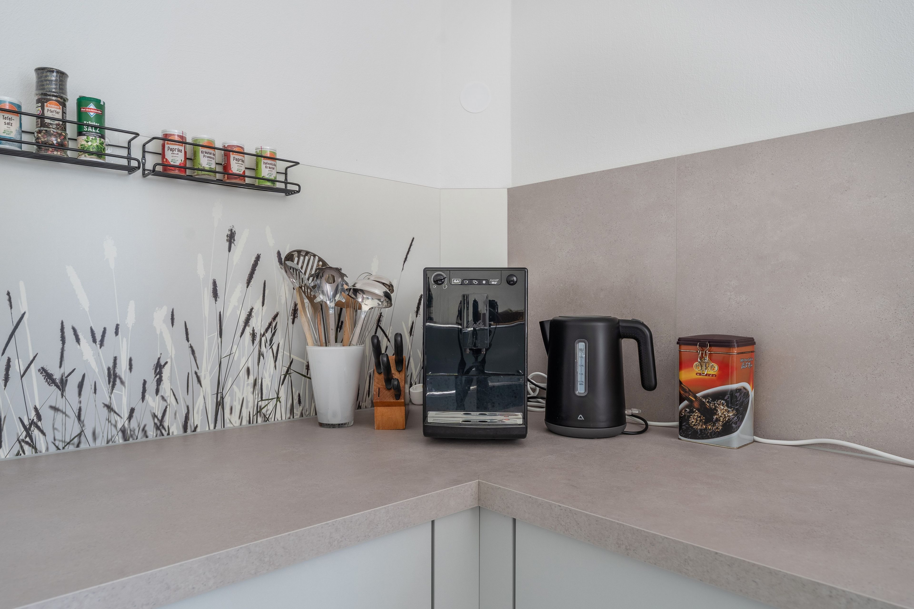 Un plan de travail de cuisine avec une machine à café, une bouilloire et un étagère à épices.