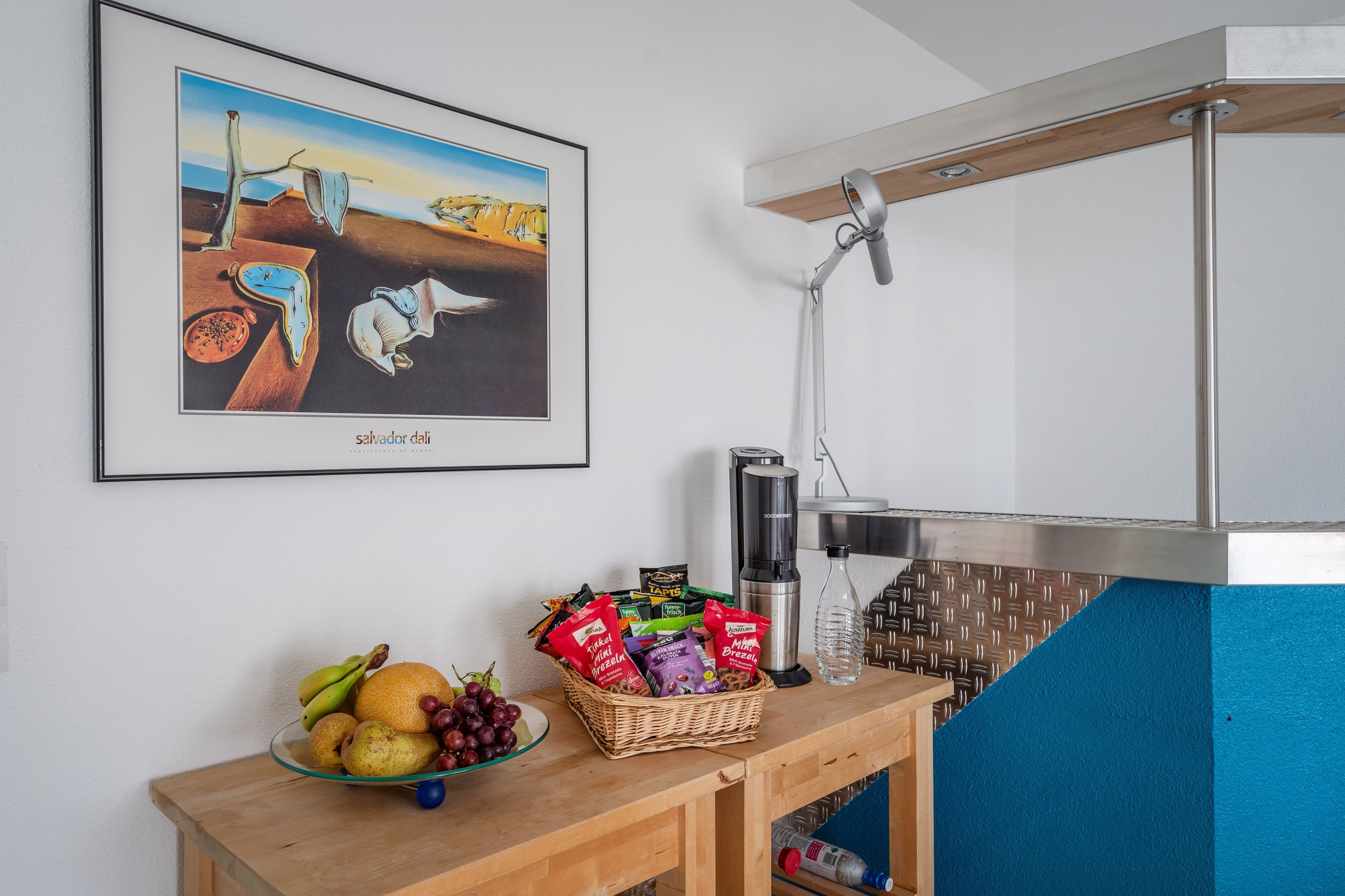 Une petite cuisine équipée d’une machine à café, d’un distributeur d’eau et d’un panier à fruits posé sur le comptoir.