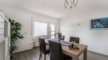 Un coin repas avec une table en bois, des chaises noires, un vase avec des fleurs et un tableau au mur.