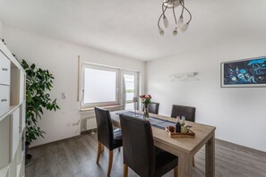A dining area with a wooden table, black chairs, a vase with flowers, and a painting on the wall.