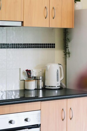 Eine Küche mit Holzschränken, einer schwarzen Arbeitsplatte, einem Wasserkocher und einer Kaffeemaschine.