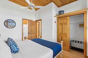 Ein Schlafzimmer mit einem Bett, einem Deckenventilator, einer Holztür und einem Kleiderschrank mit Kleidung.