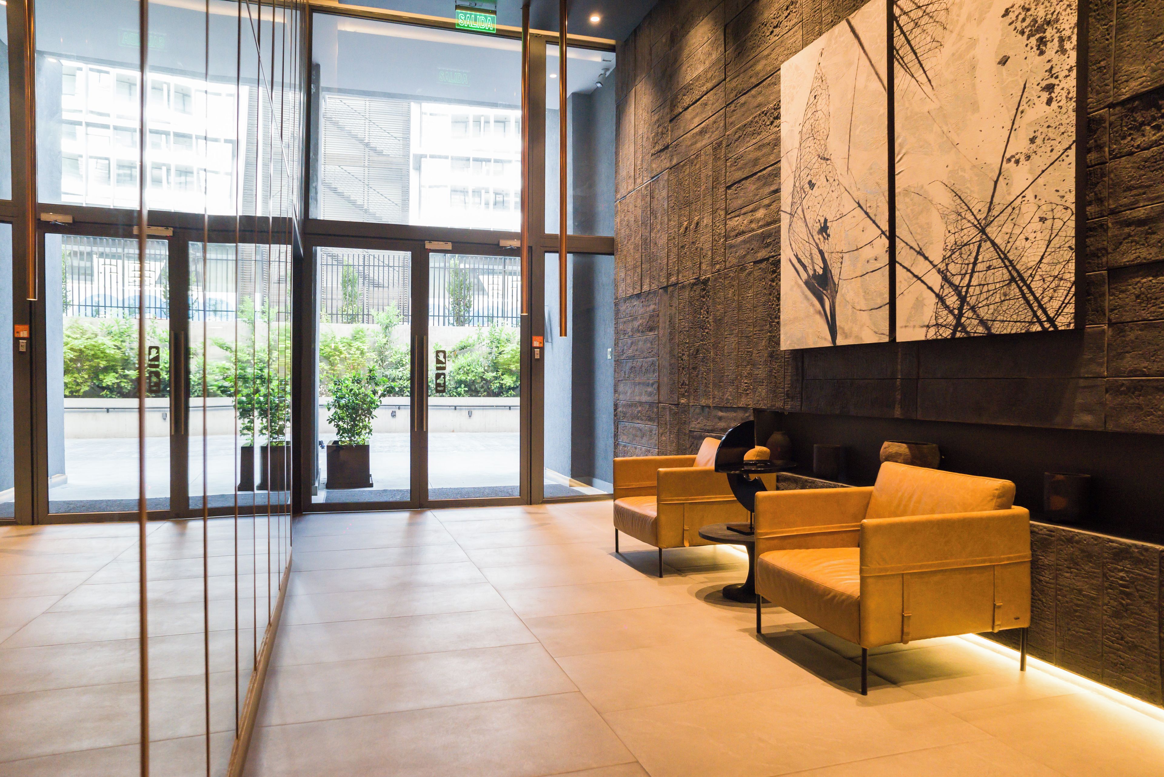 A reception area with a modern design, featuring a large glass door entrance, a seating area with two sofas, and a wall-mounted abstract art piece.