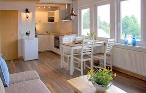 A compact kitchen with white cabinetry, a dining area with a wooden table and chairs, and a view of greenery through the windows. - 2 bedroom lovely apartment in Röbel (Röbel)